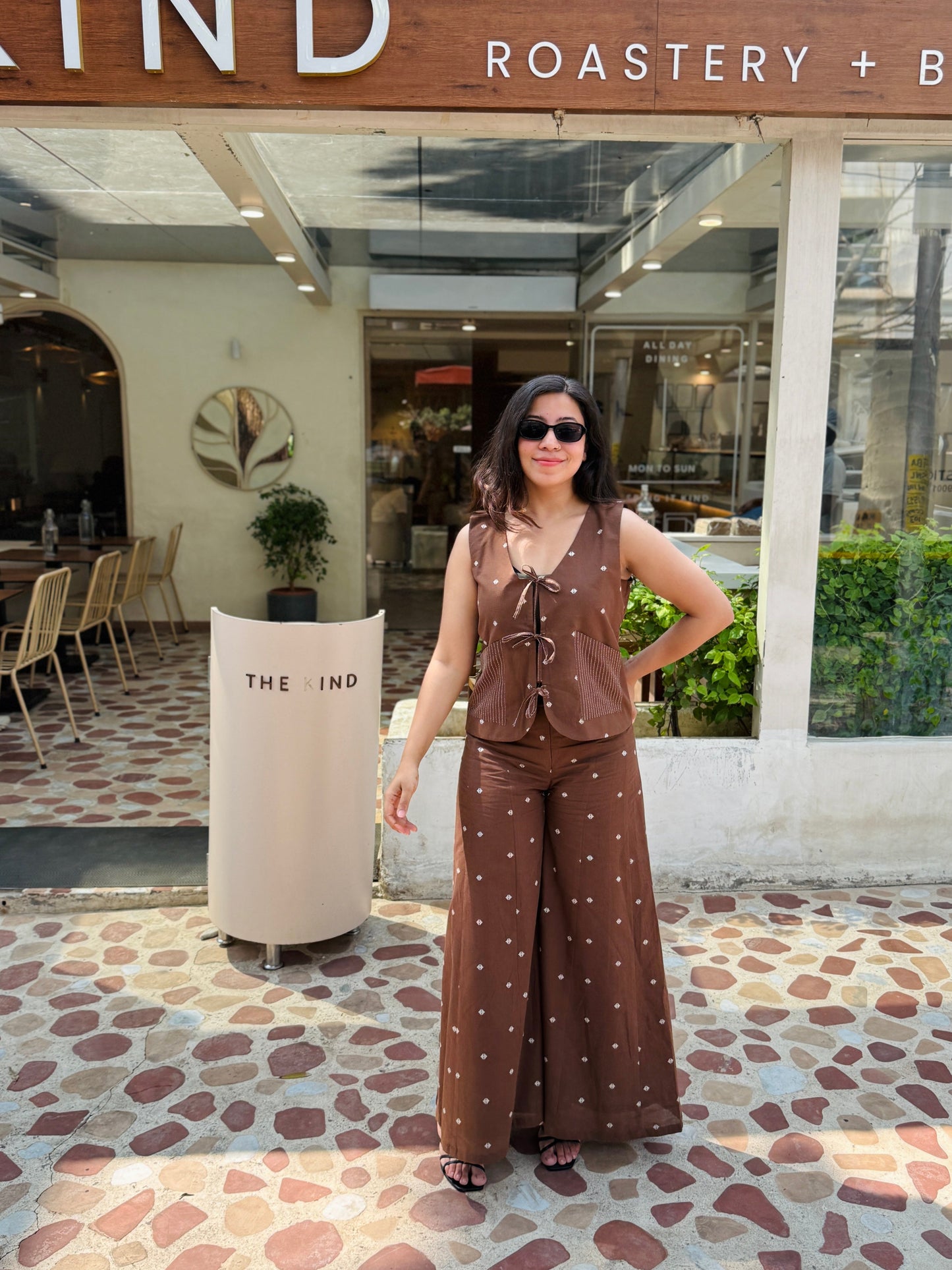 Woman in a brown outfit standing in front of 'The Pizza Kind' restaurant.