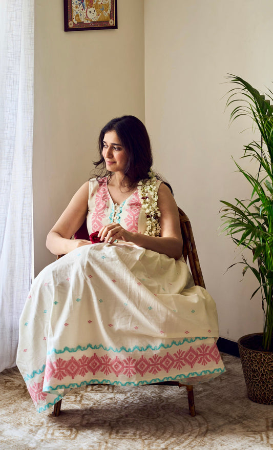 Woman in a traditional outfit sitting on a chair next to a potted plant indoors.